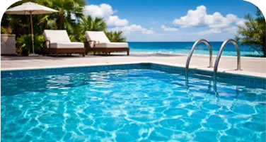 Poolside scene with two lounge chairs under an umbrella, turquoise pool water and a beach/ocean in the background.