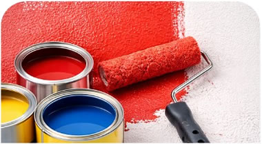 Open cans of red, yellow, and blue paint with a roller applying red paint to a white wall.